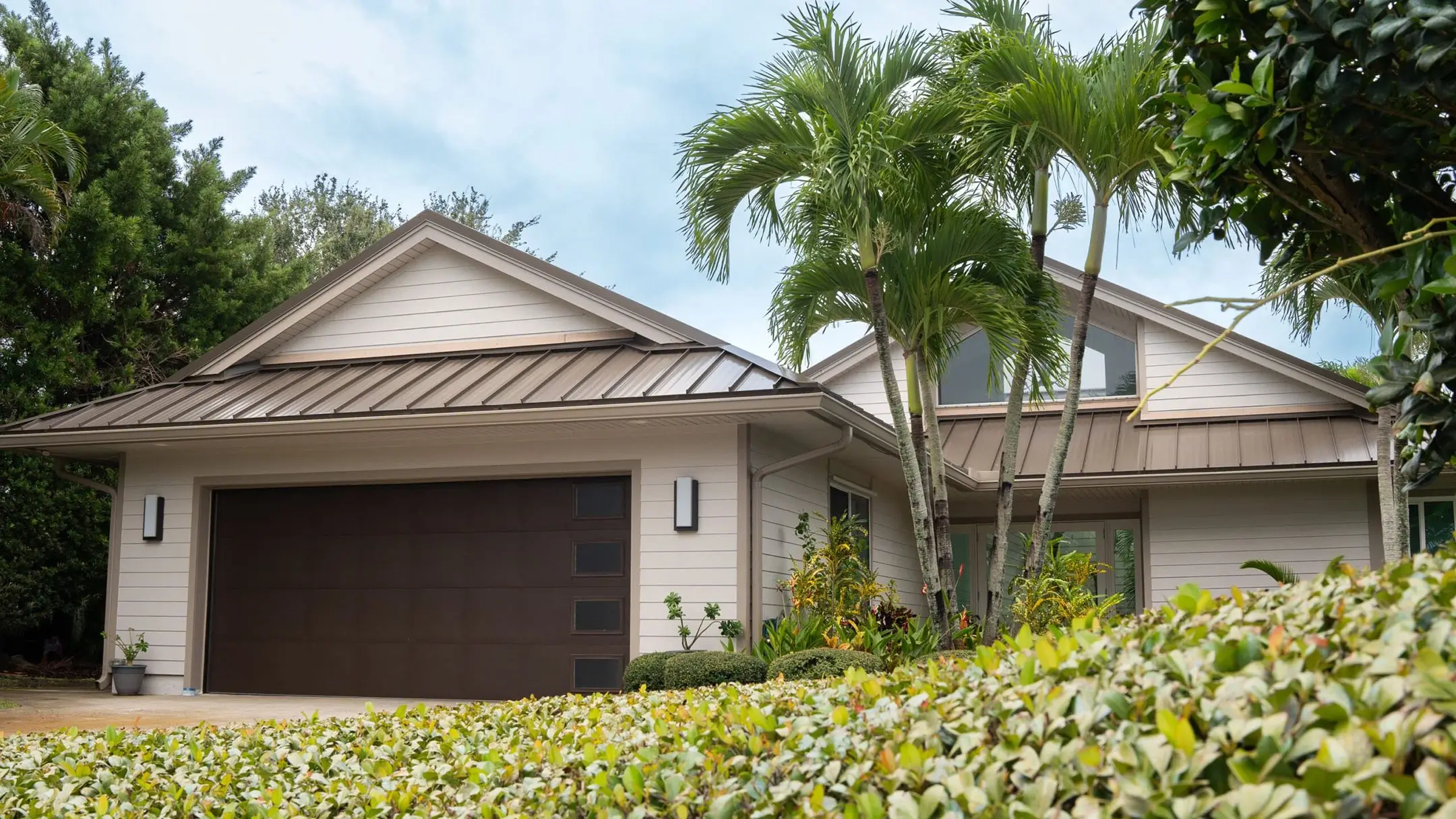 House with a light gray metal gable roof and palms