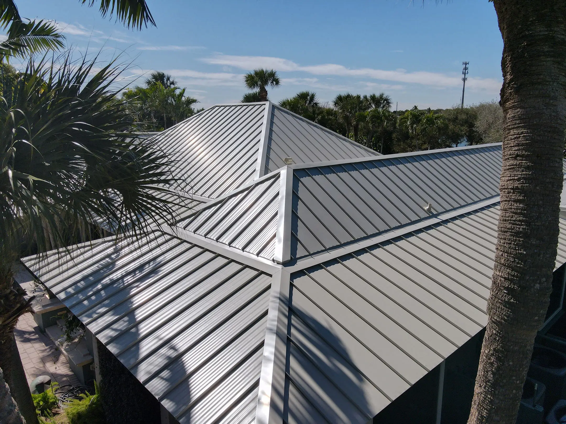 Silver standing seam metal hip roof on a Florida home among palms
