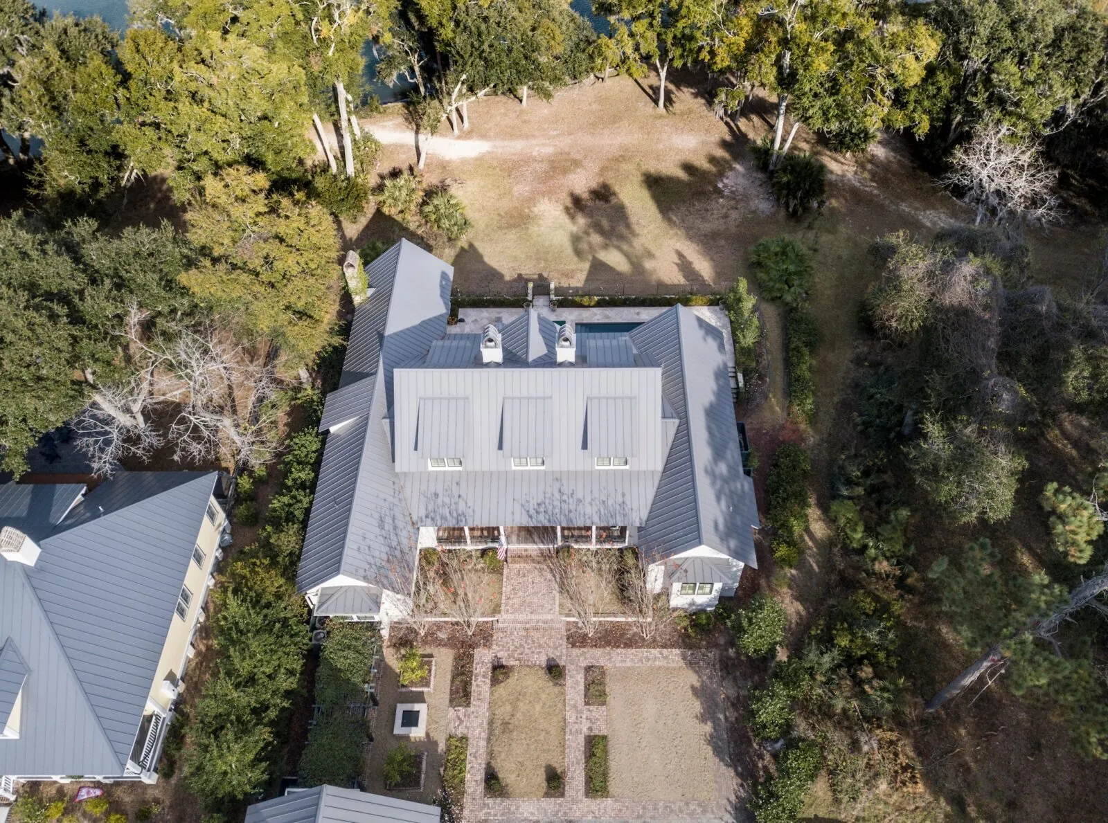 Aerial view of a home with a standing seam metal roof on a wooded lot
